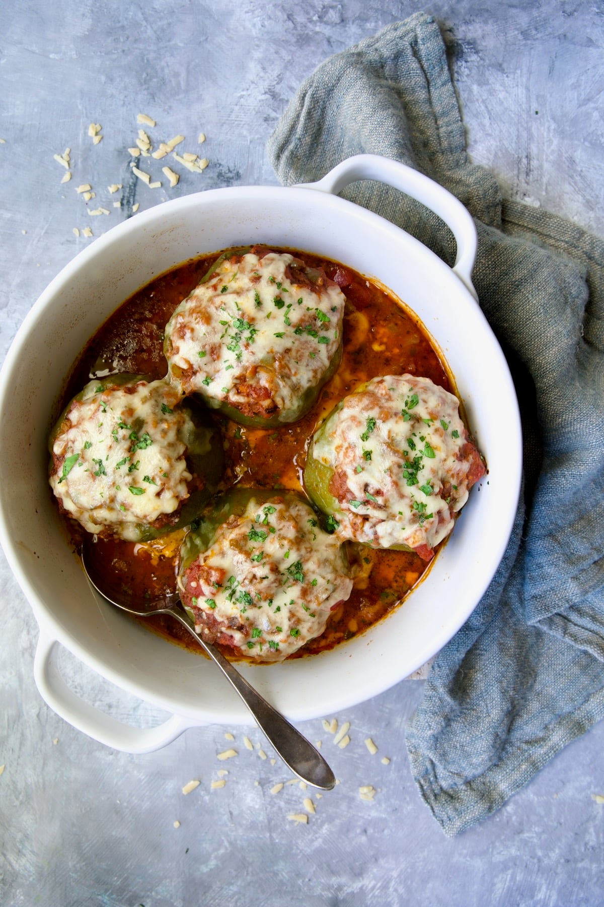 Four Italian Stuffed Peppers in deep white round baking dish with serving spoon and blue napkin.