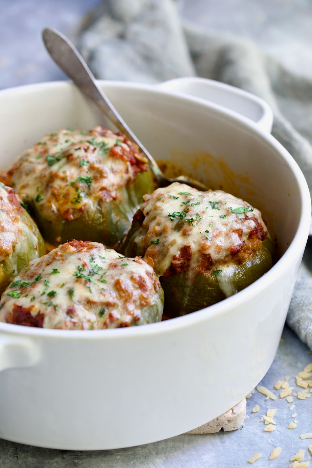 Four Italian Stuffed Peppers in deep white round baking dish with serving spoon.