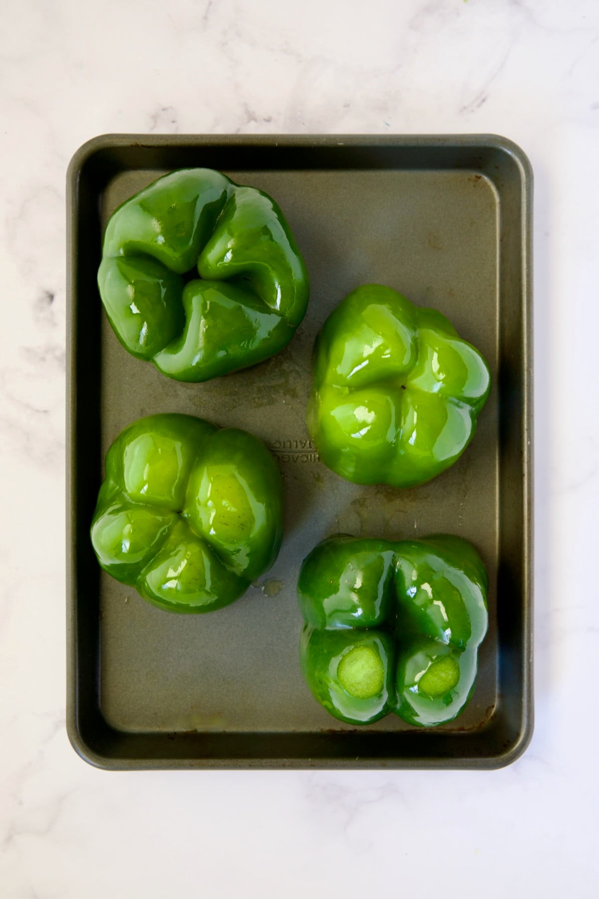 Four green bell peppers turned upside down on rimmed sheet pan.