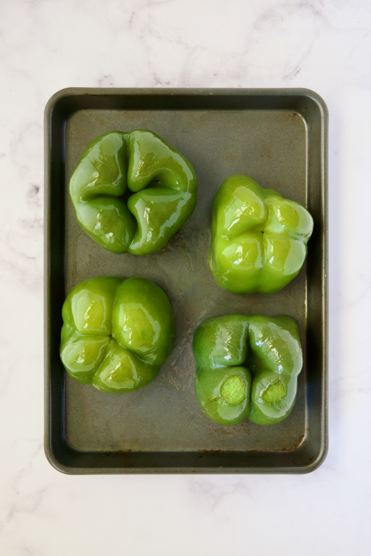 Four green bell peppers turned upside down after being roasted for 15 minutes on rimmed sheet pan.