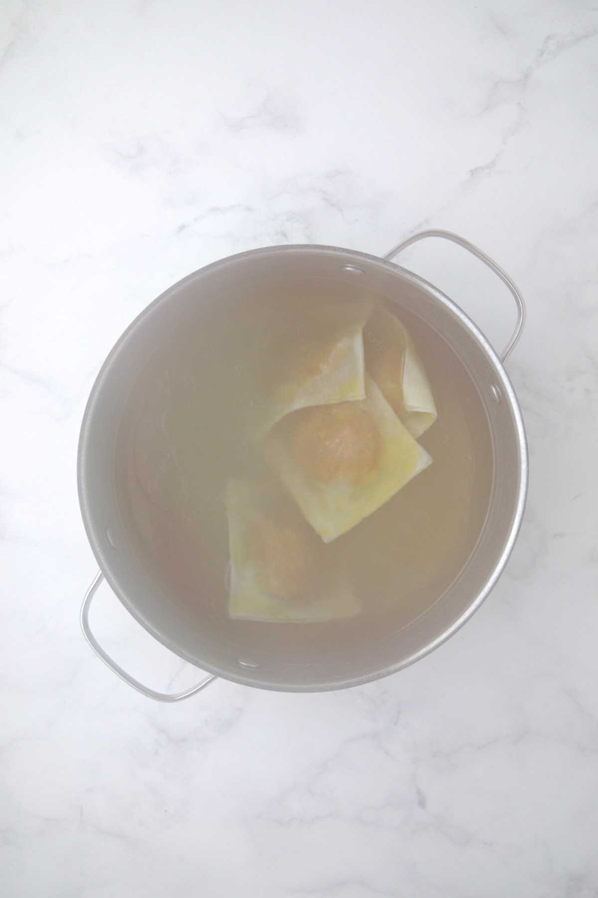 Steamy stainless steel pot with four cooked ravioli.