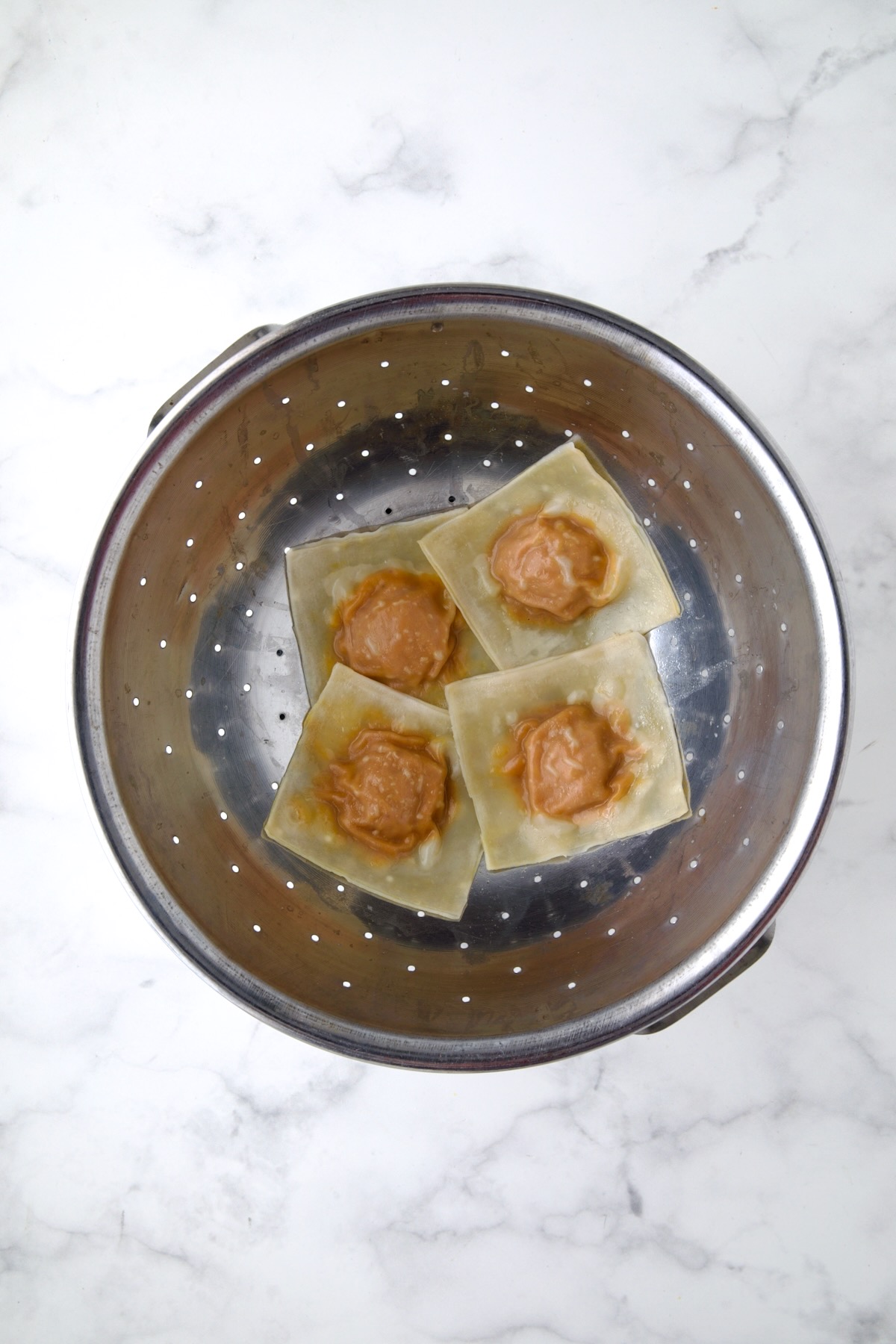 Four cooked pumpkin ravioli in stainless steel colander.