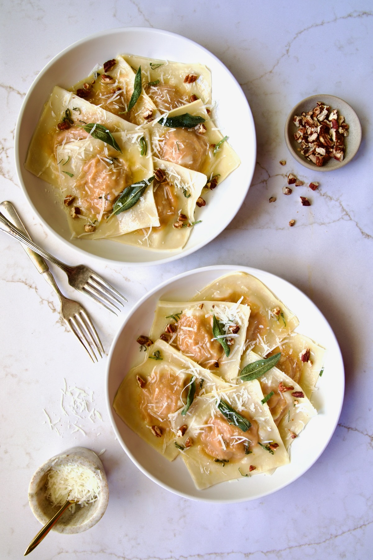 Two bowls of Pumpkin Ravioli with Sage Brown Butter garnished with toasted pecans and fried sage leaves.