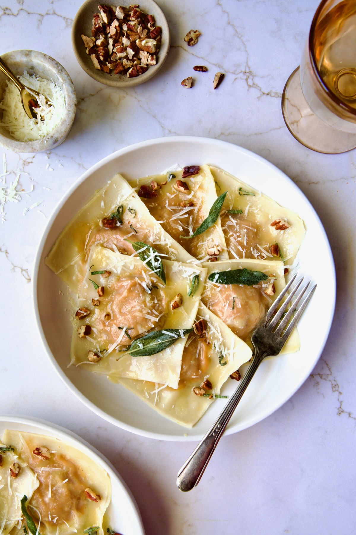 Pumpkin Ravioli with Sage Brown Butter in white pasta bowl garnished with toasted pecans and fried sage leaves.