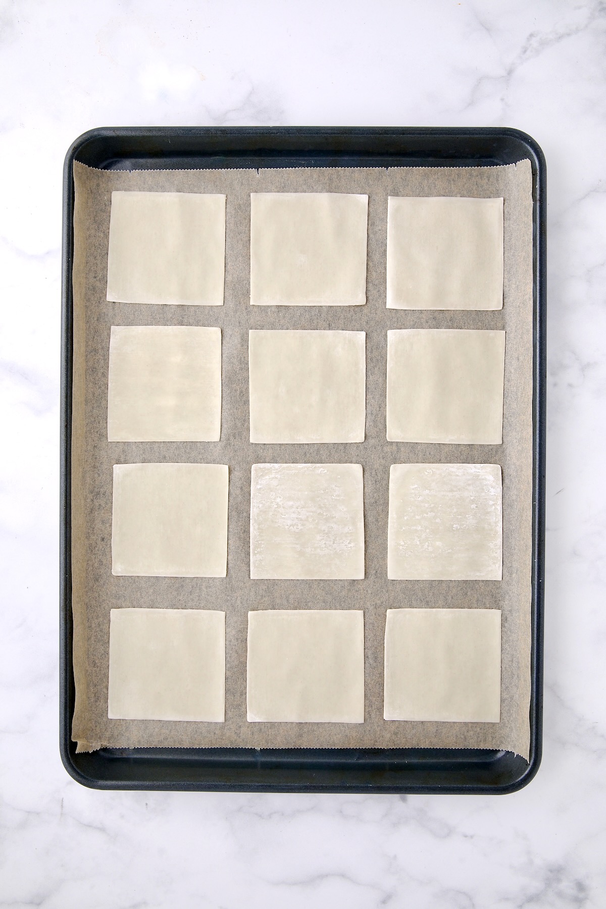 12 wonton skins on a parchment paper lined rimmed baking sheet.