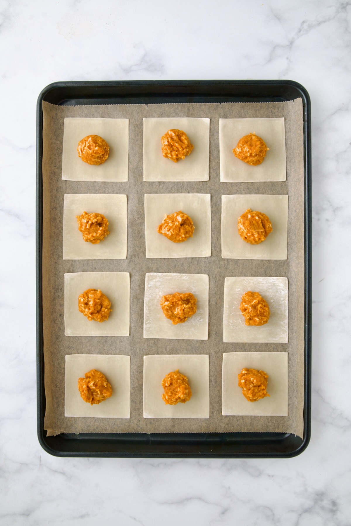 12 wonton skins on parchment paper lined rimmed baking sheet with equal amounts of the pumpkin and cheese combination on each.