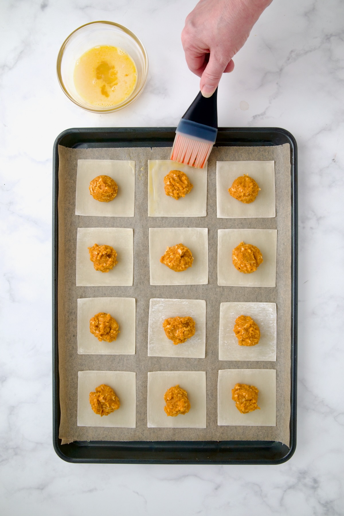 Hand of a person brushing the wonton skins with beaten egg.