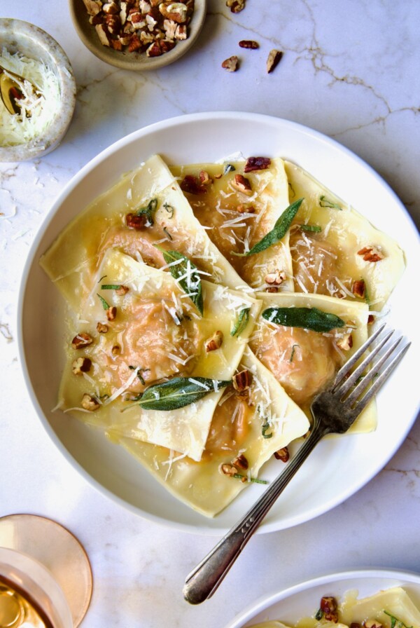 Pumpkin Ravioli with Sage Brown Butter in white pasta bowl garnished with toasted pecans and fried sage leaves.
