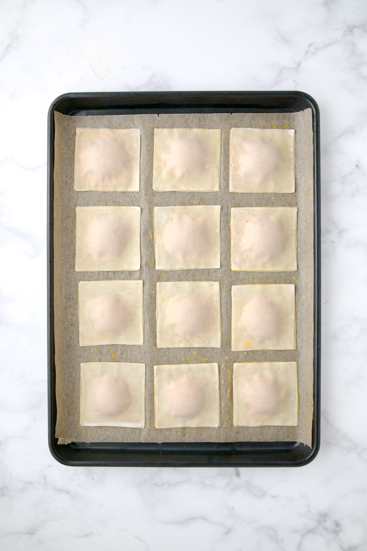12 sealed pumpkin ravioli on parchment paper-lined rimmed baking sheet.