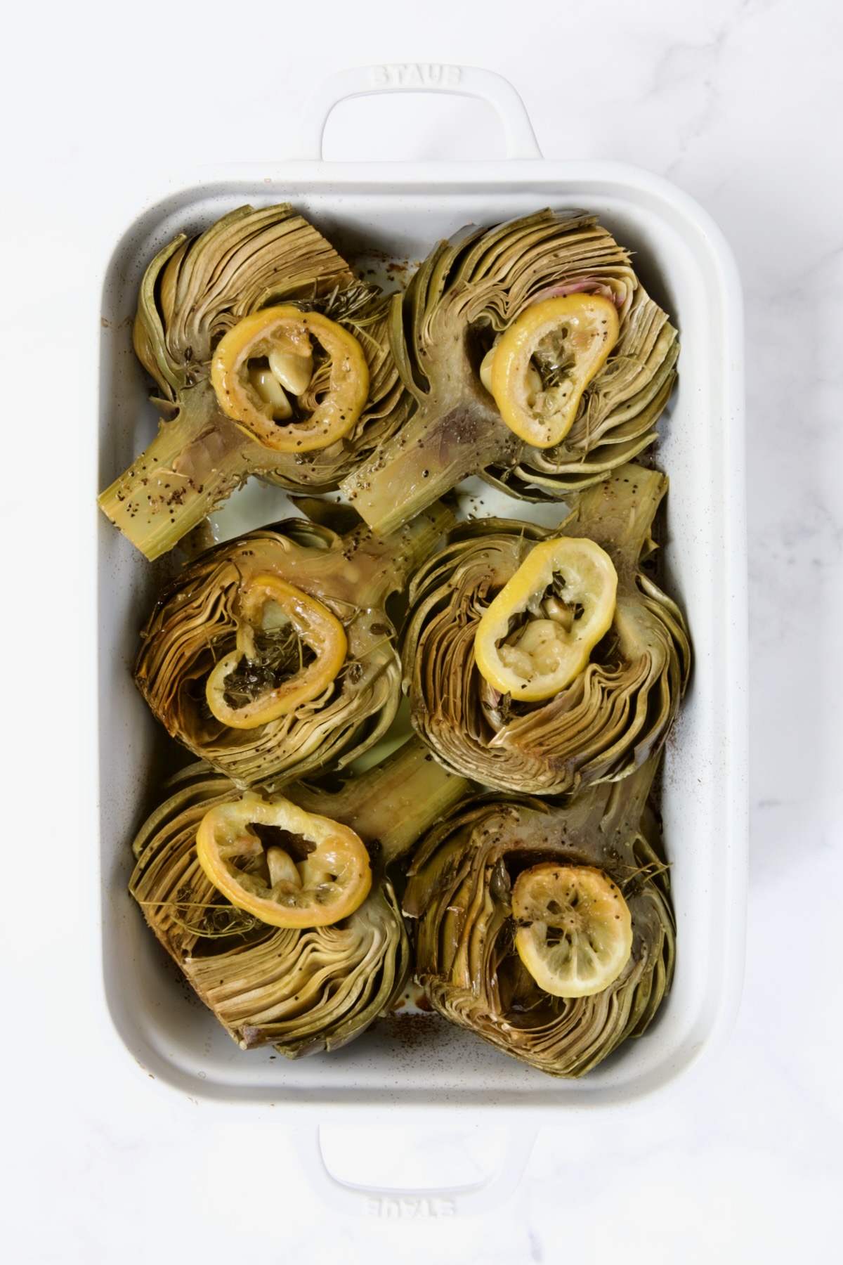 Six artichoke halves in a white roasting pan turned cut side up after being roasted.