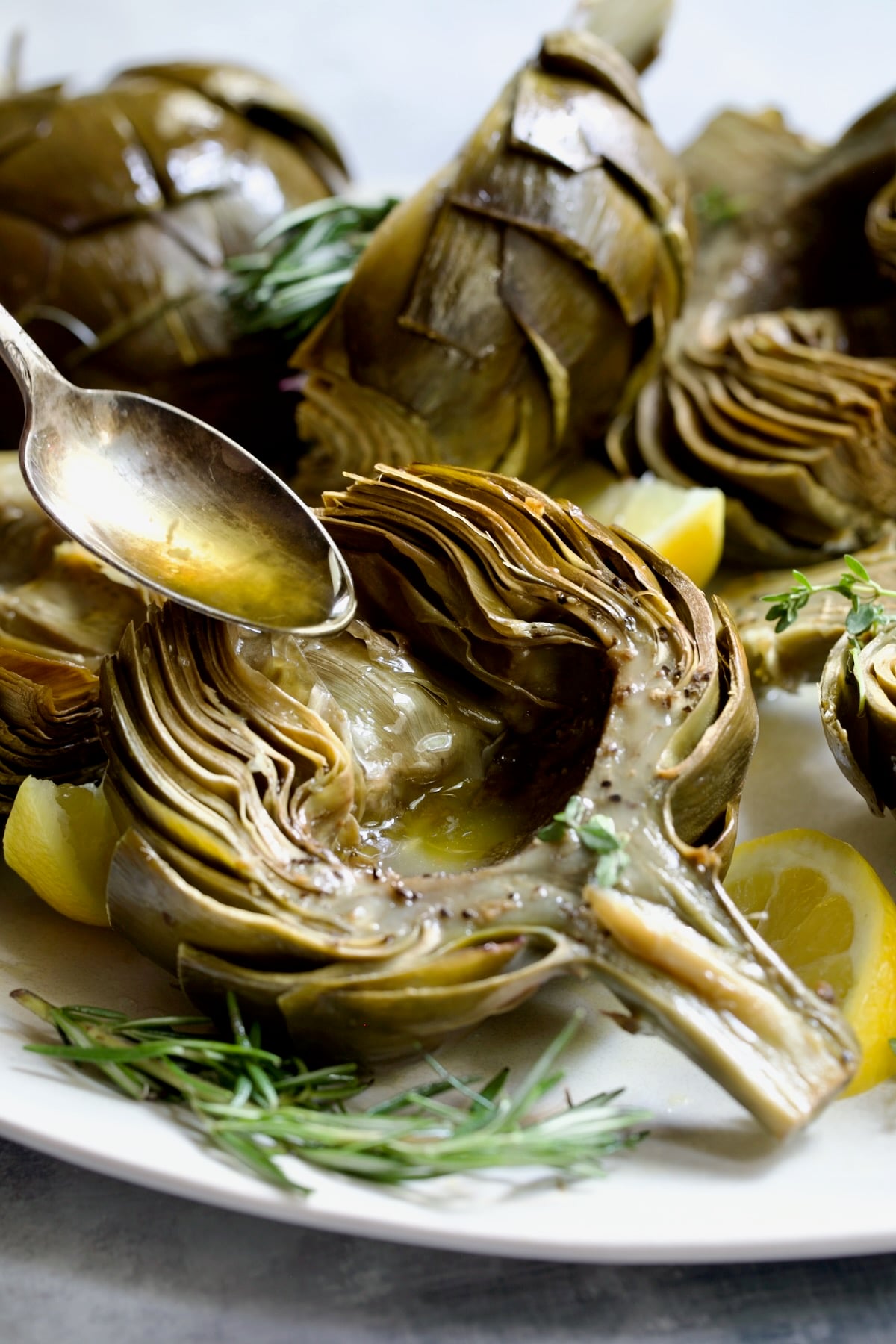 Butter being poured into the well of a roasted artichoke half.