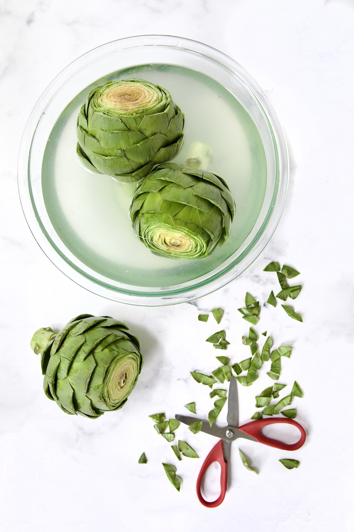 Three artichokes being trimmed with two in lemon water.