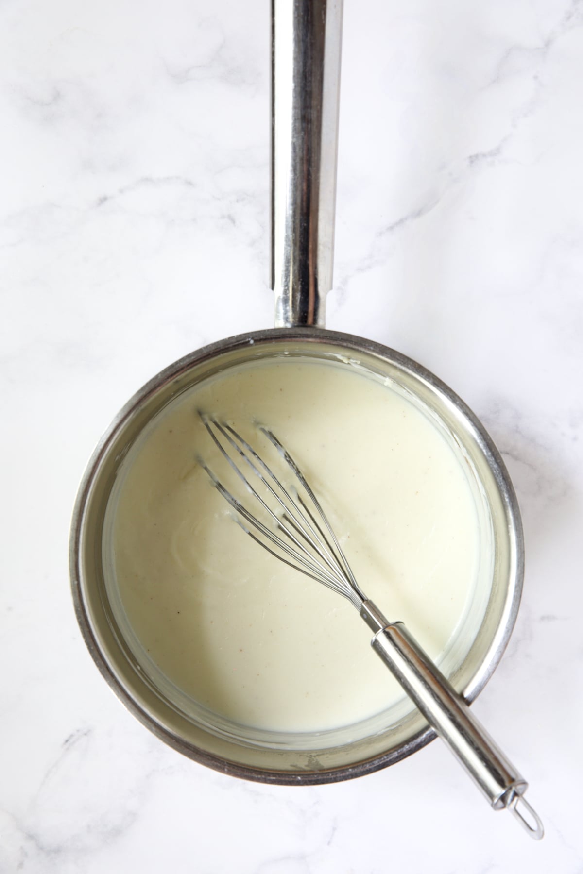 Bechamel sauce in stainless steel saucepan with wire whisk.
