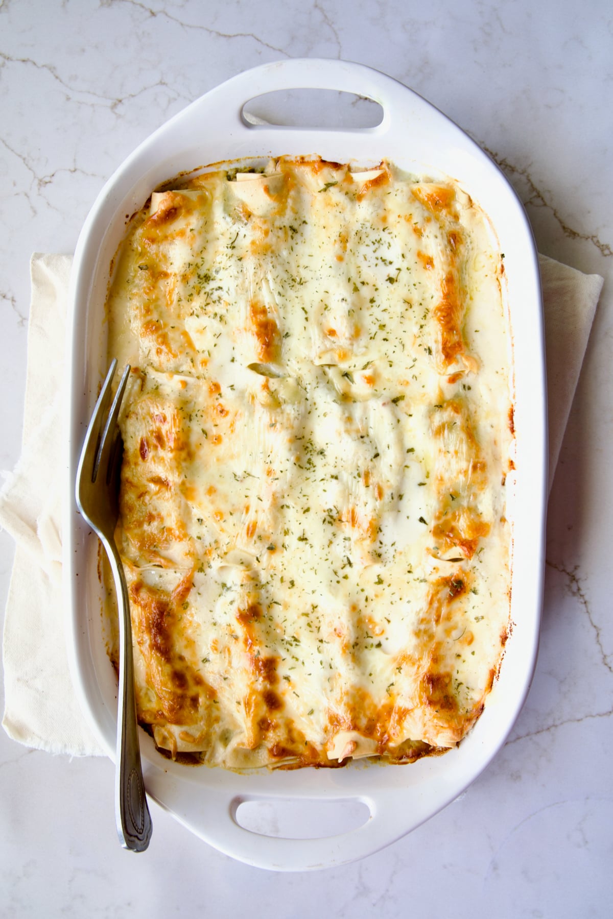 Cannelloni with Chicken, Spinach and Artichokes in white baking dish with serving fork.