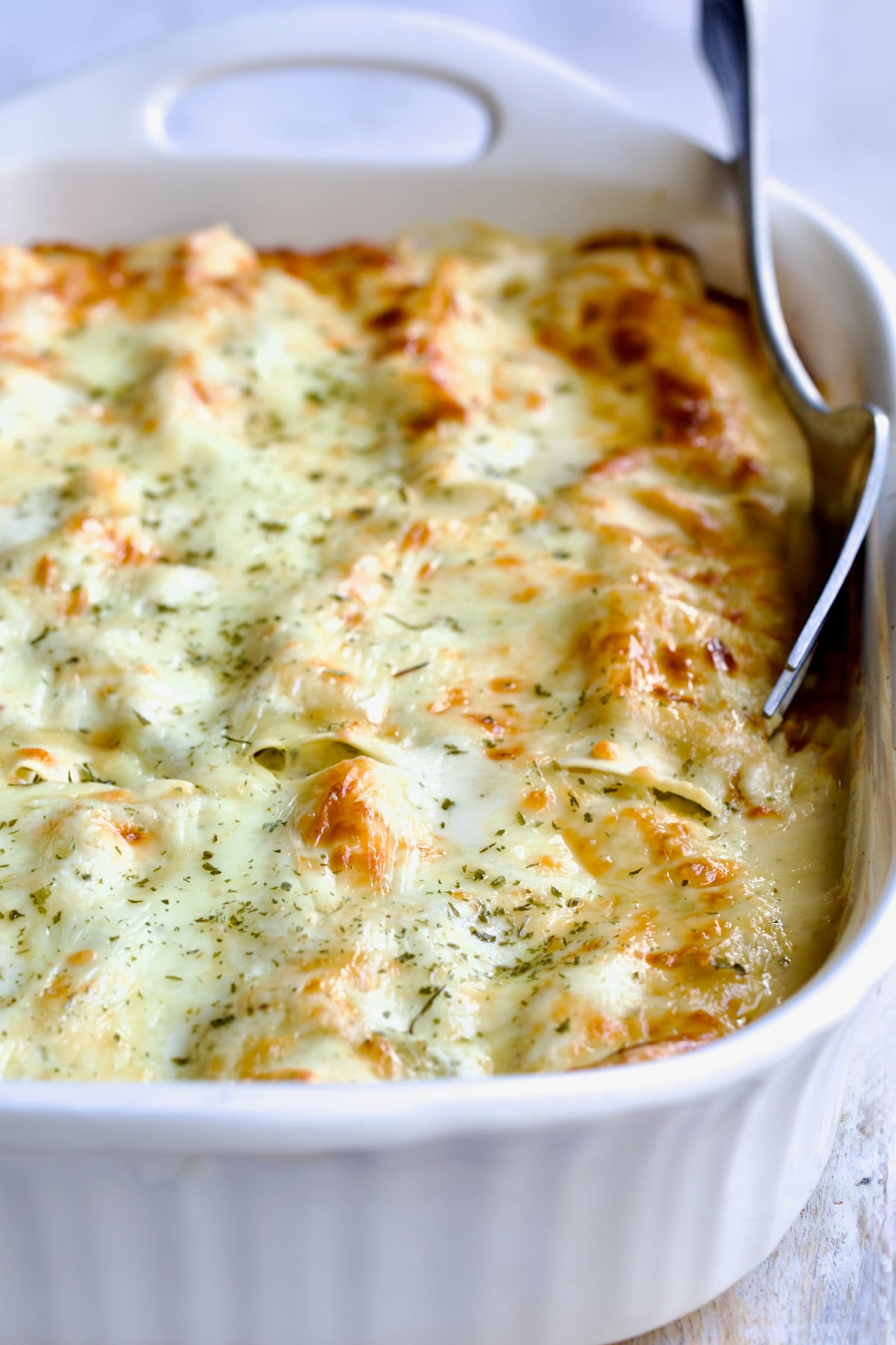 Cannelloni with Chicken, Spinach and Artichokes in white baking dish with serving fork.