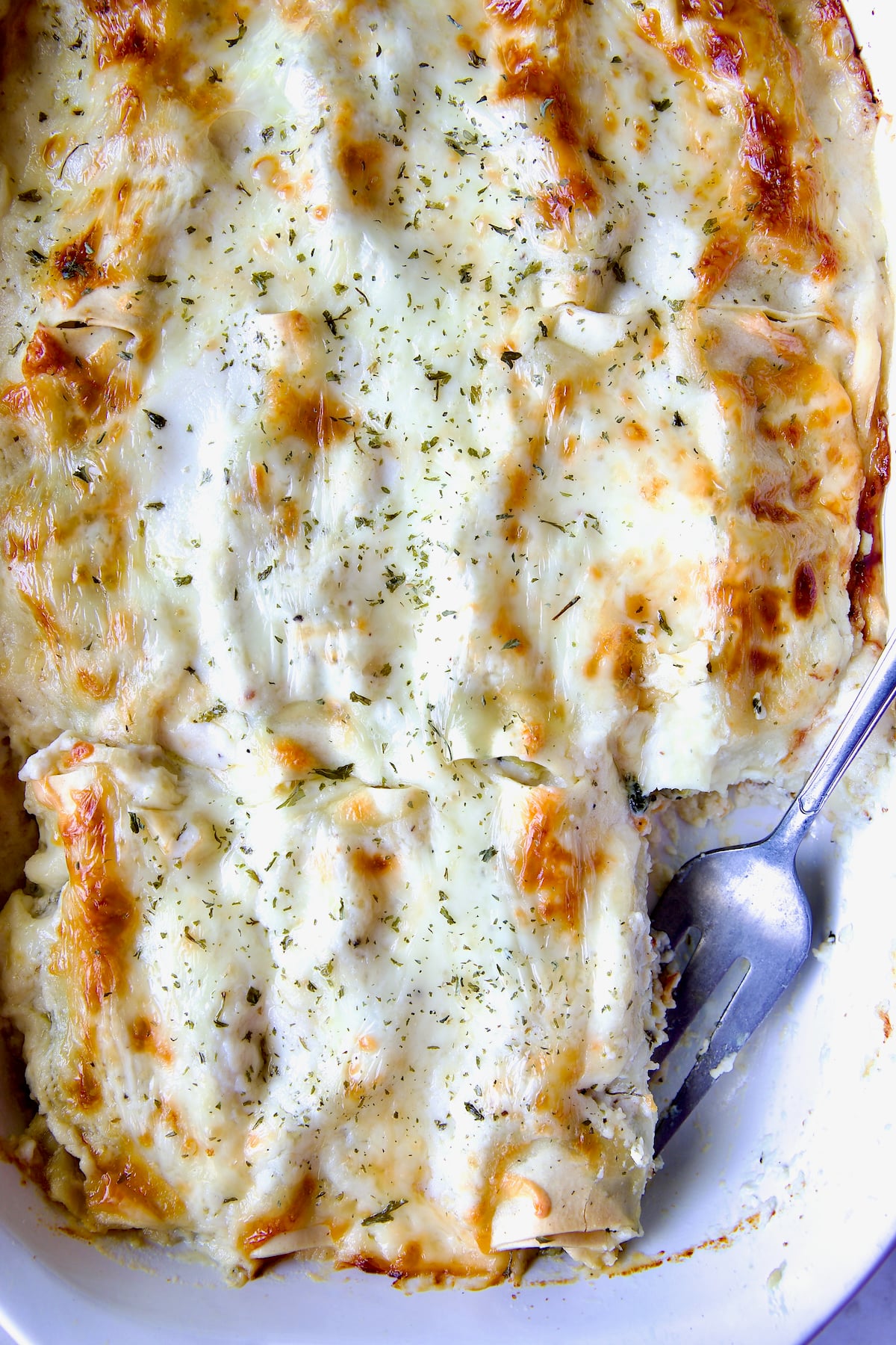 Cannelloni with Chicken, Spinach and Artichokes in white baking dish with one piece missing and serving fork in its place.