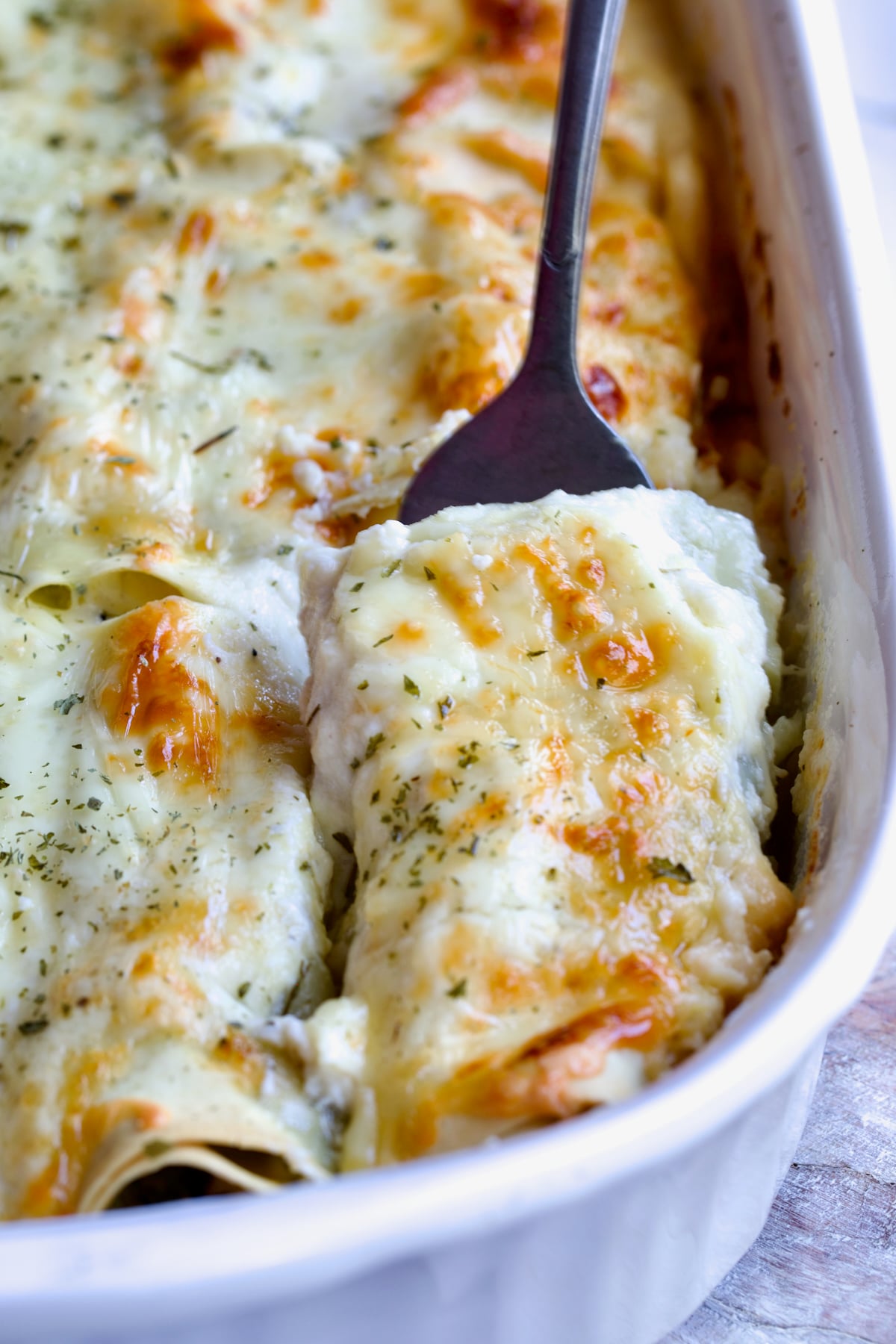 Serving fork picking up a Cannelloni with Chicken, Spinach and Artichokes from white baking dish.