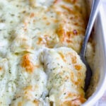 Serving fork picking up a Cannelloni with Chicken, Spinach and Artichokes from white baking dish.