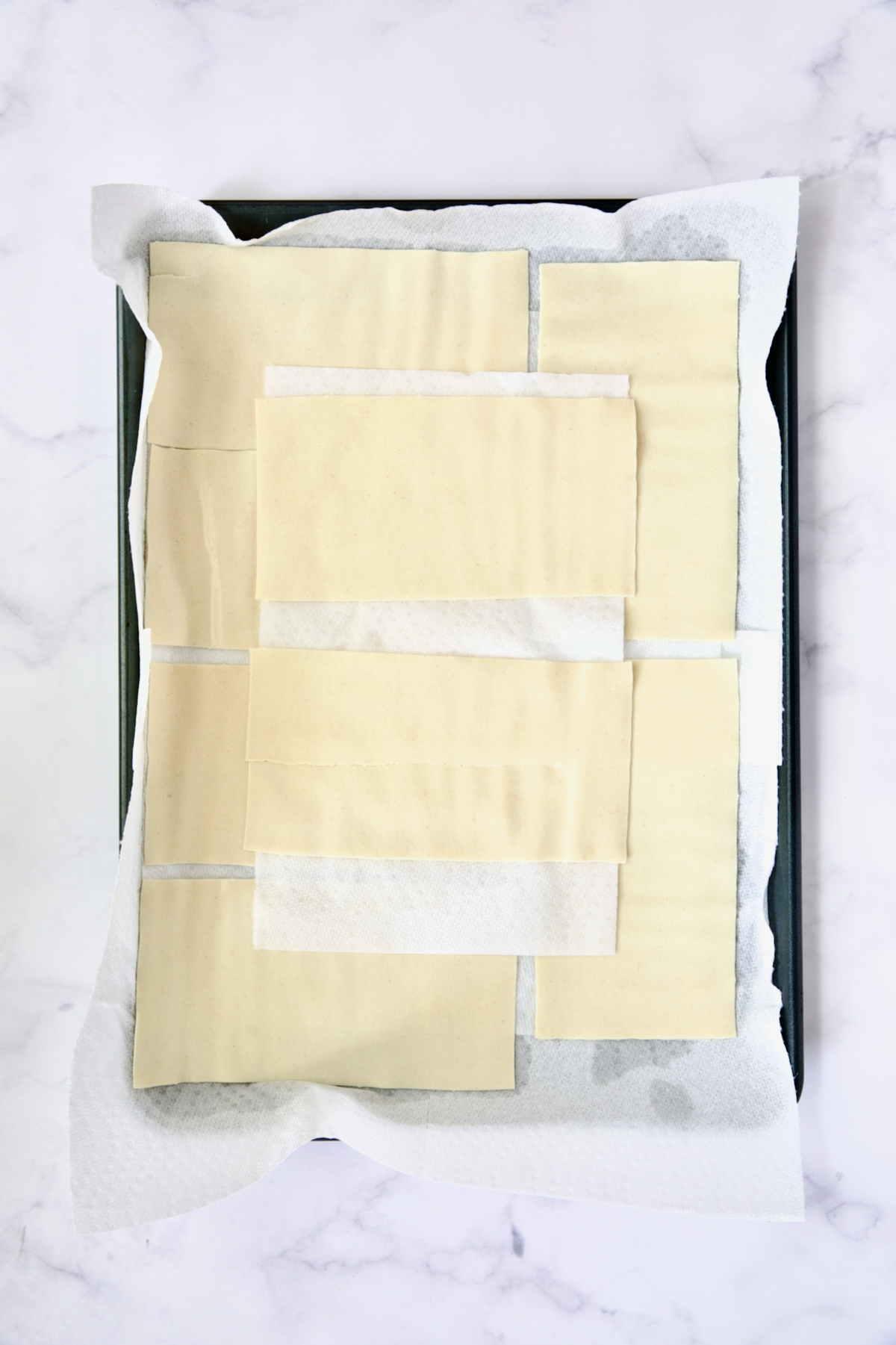 12 flat lasagna sheets on paper towels on rimmed sheet pan.