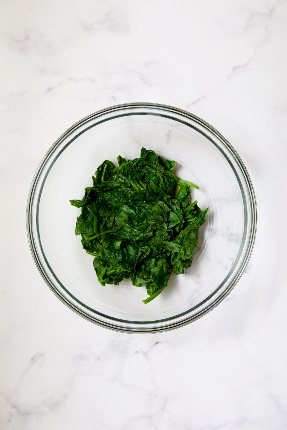 Cooked spinach in glass bowl.