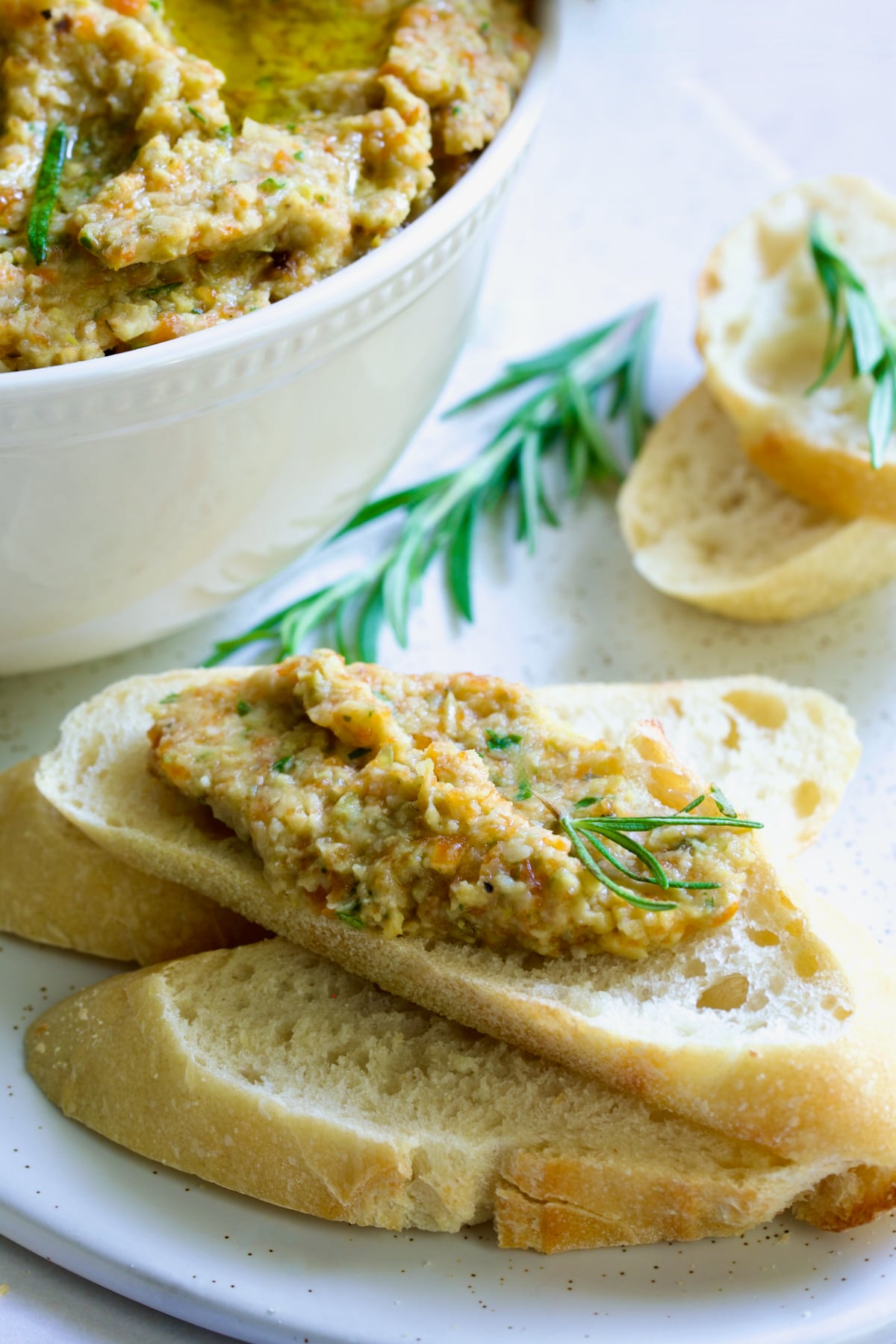 Slices of bread with the tapenade spread on one garnished with fresh rosemary.