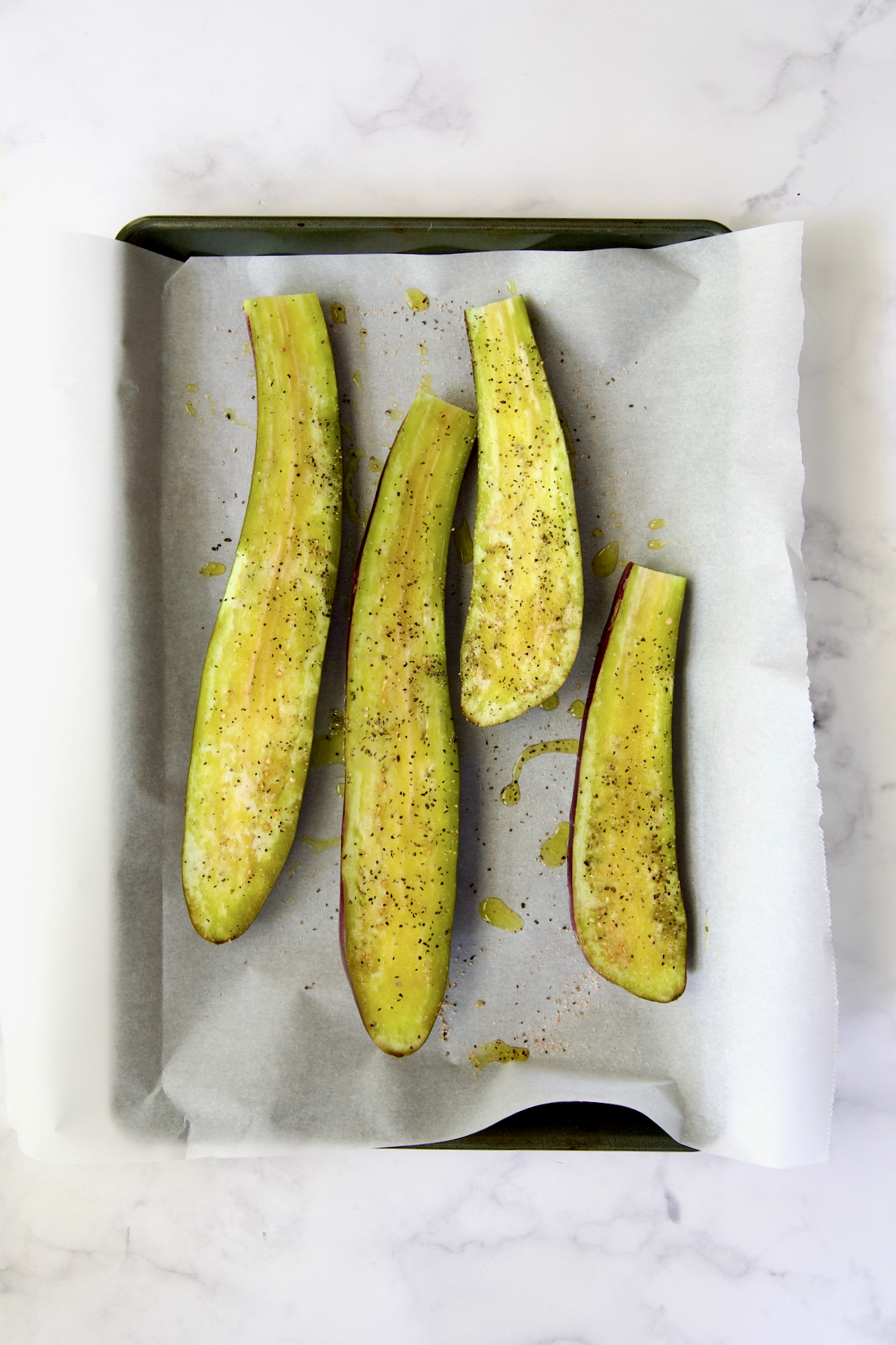 Four slices of Japanese eggplant cut side up brushed with olive oil and sprinkled with salt and black pepper on parchment paper-lined rimmed baking sheet.