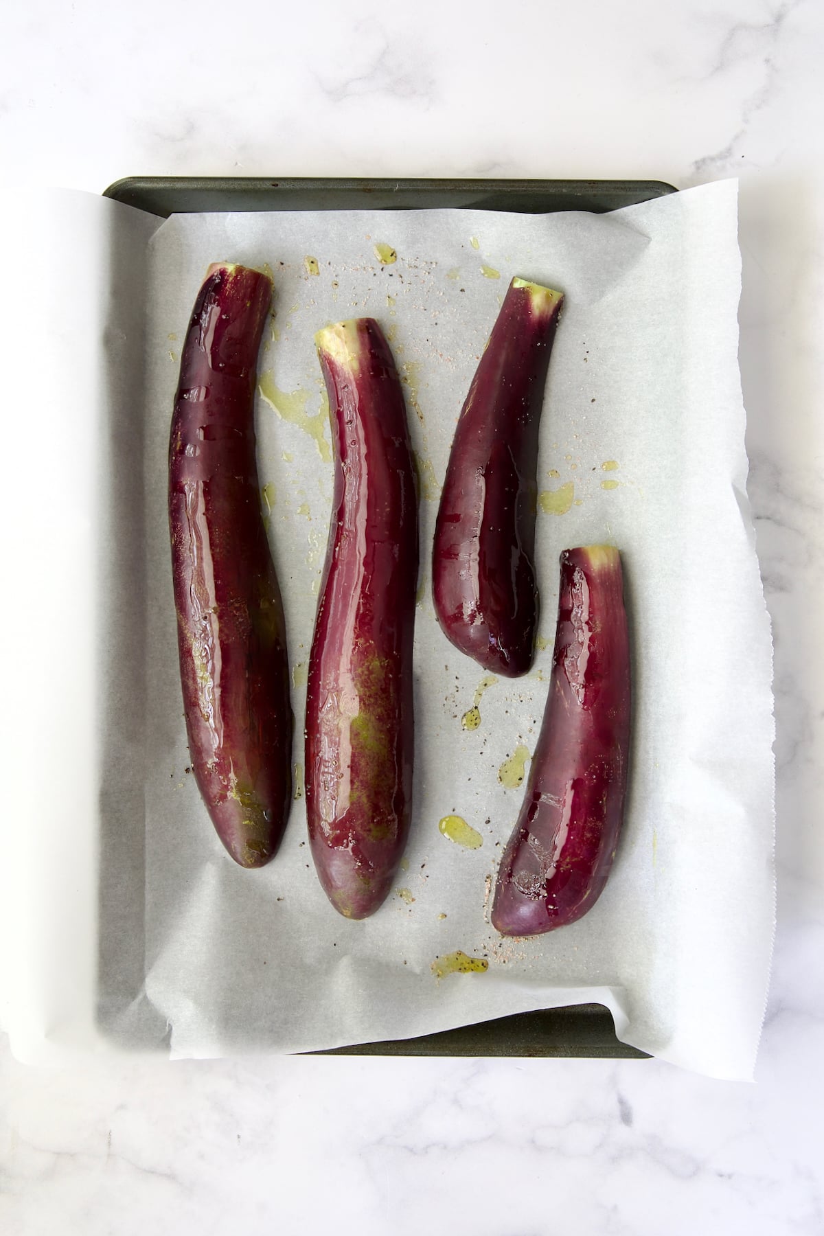 Four slices of Japanese eggplant cut side down brushed with olive oil and sprinkled with salt and black pepper on parchment paper-lined rimmed baking sheet.