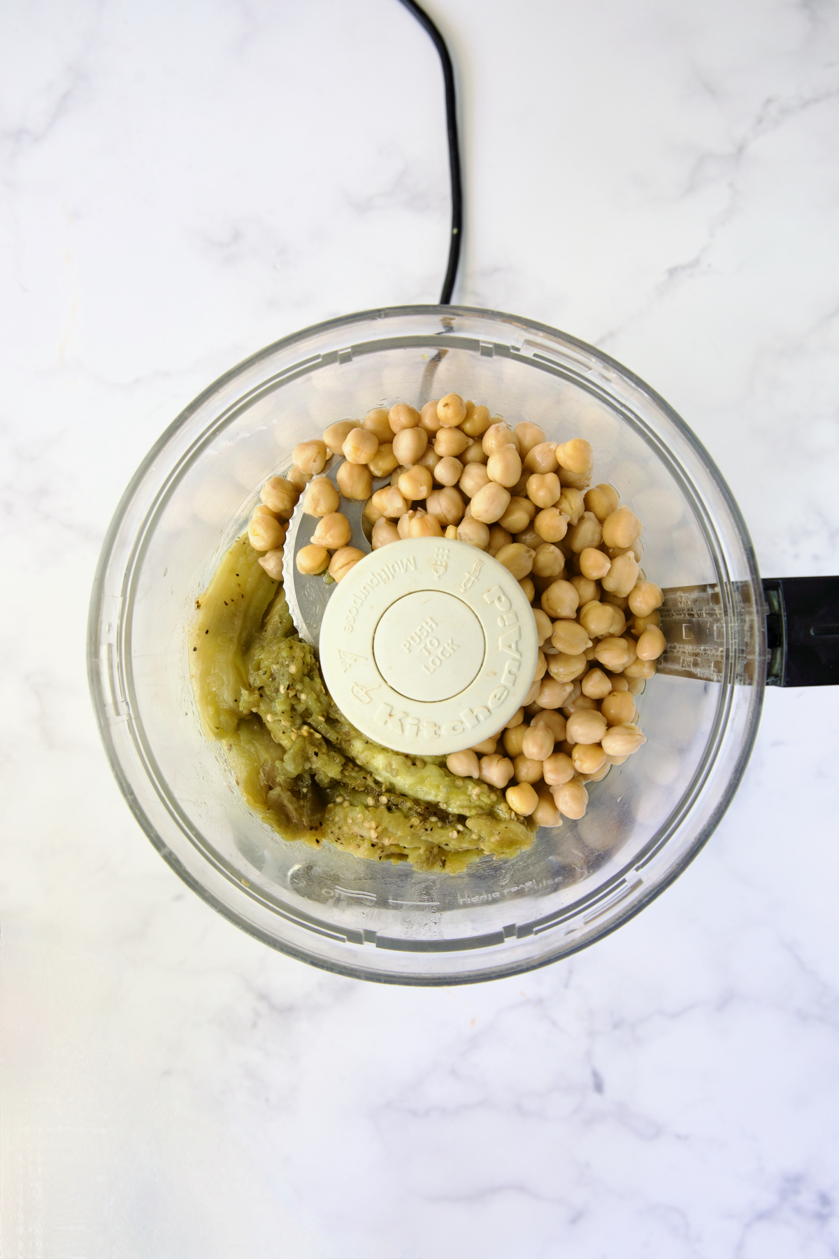 Chickpeas and cooked eggplant pulp in bowl of food processor.