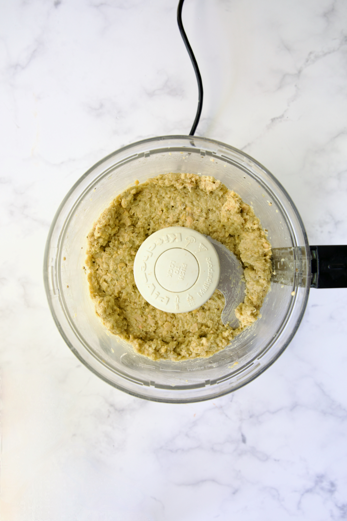 Pureed chickpeas and eggplant in bowl of food processor.