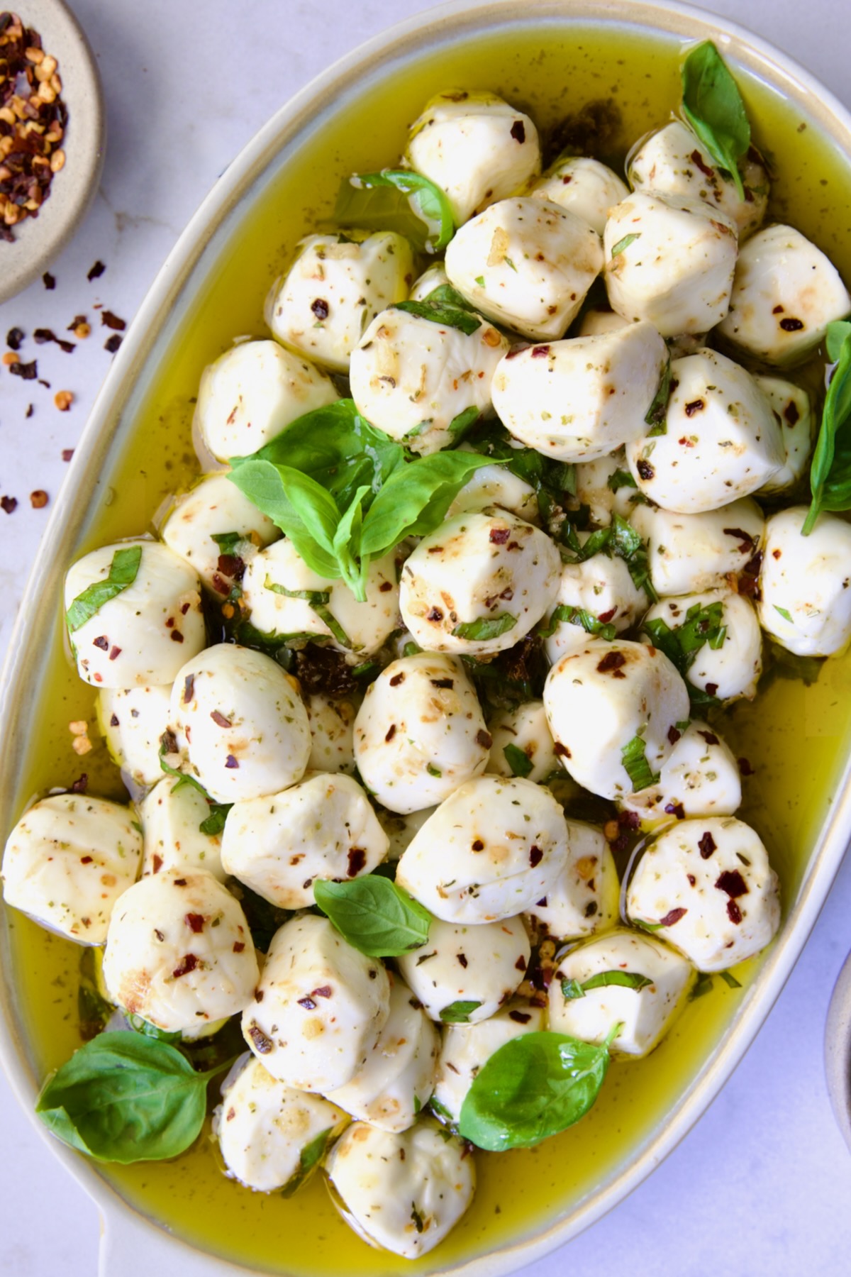 Marinated Mozzarella Balls on oval platter garnished with fresh basil leaves.