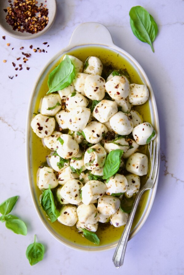 Marinated Mozzarella Balls on oval platter garnished with fresh basil leaves.
