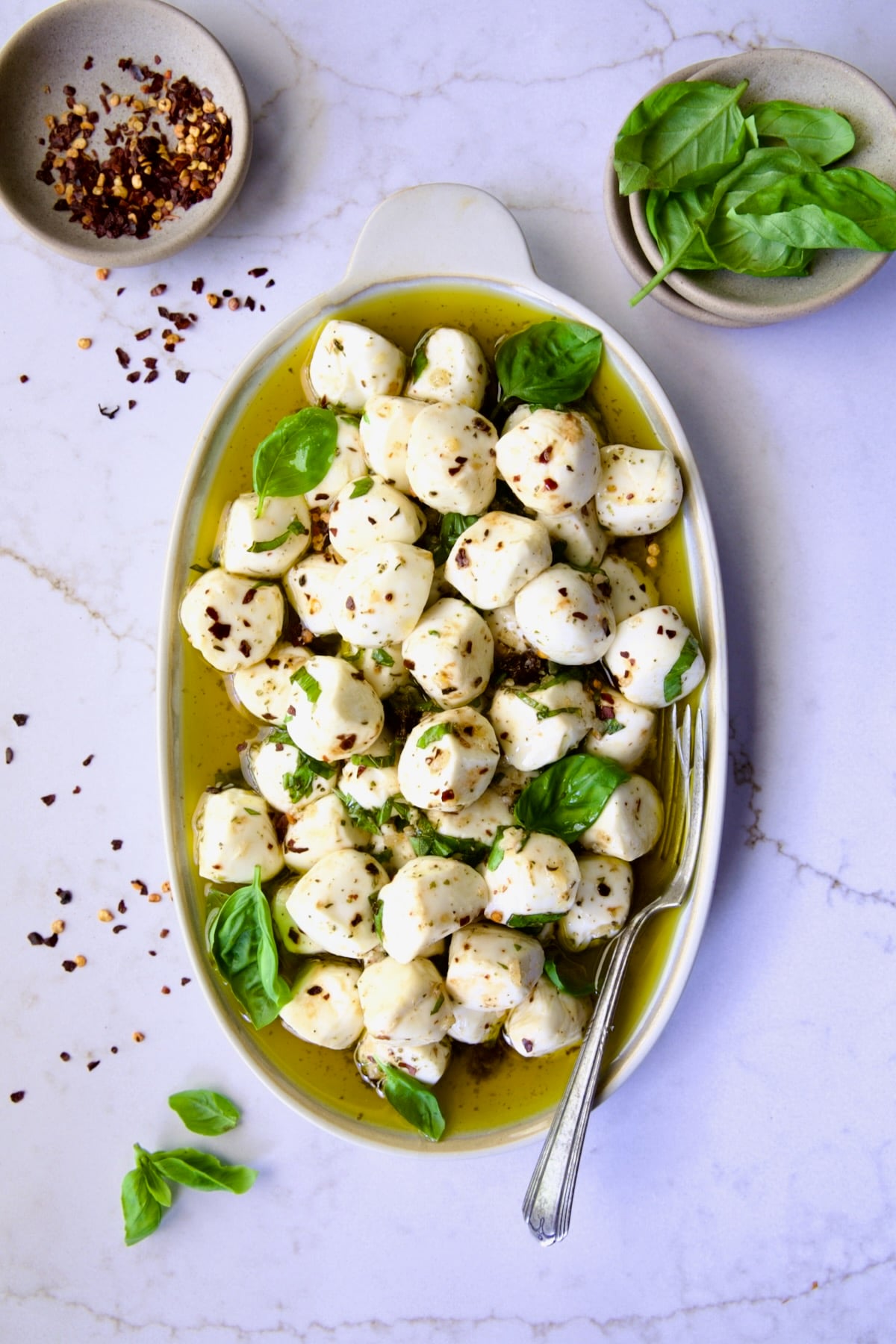Marinated Mozzarella Balls on oval platter garnished with fresh basil leaves.