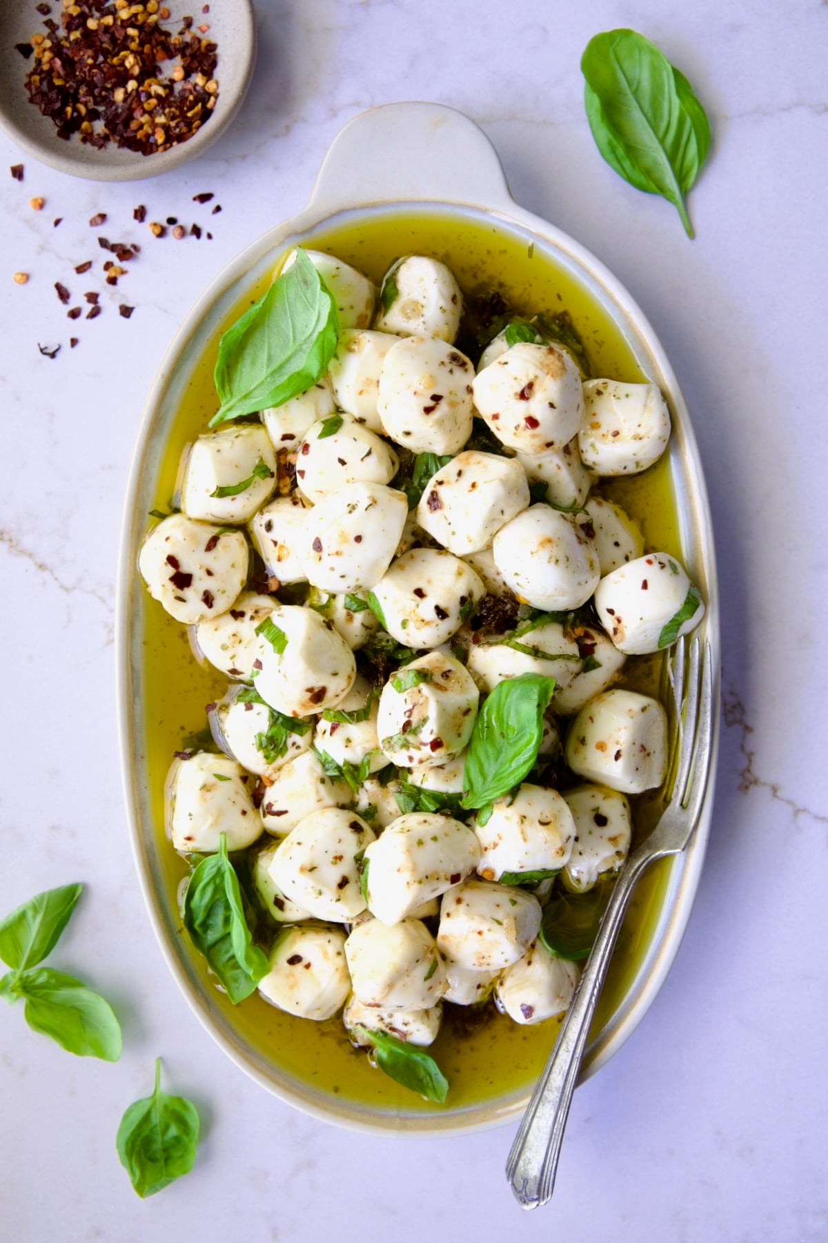 Marinated Mozzarella Balls on oval platter garnished with fresh basil leaves.