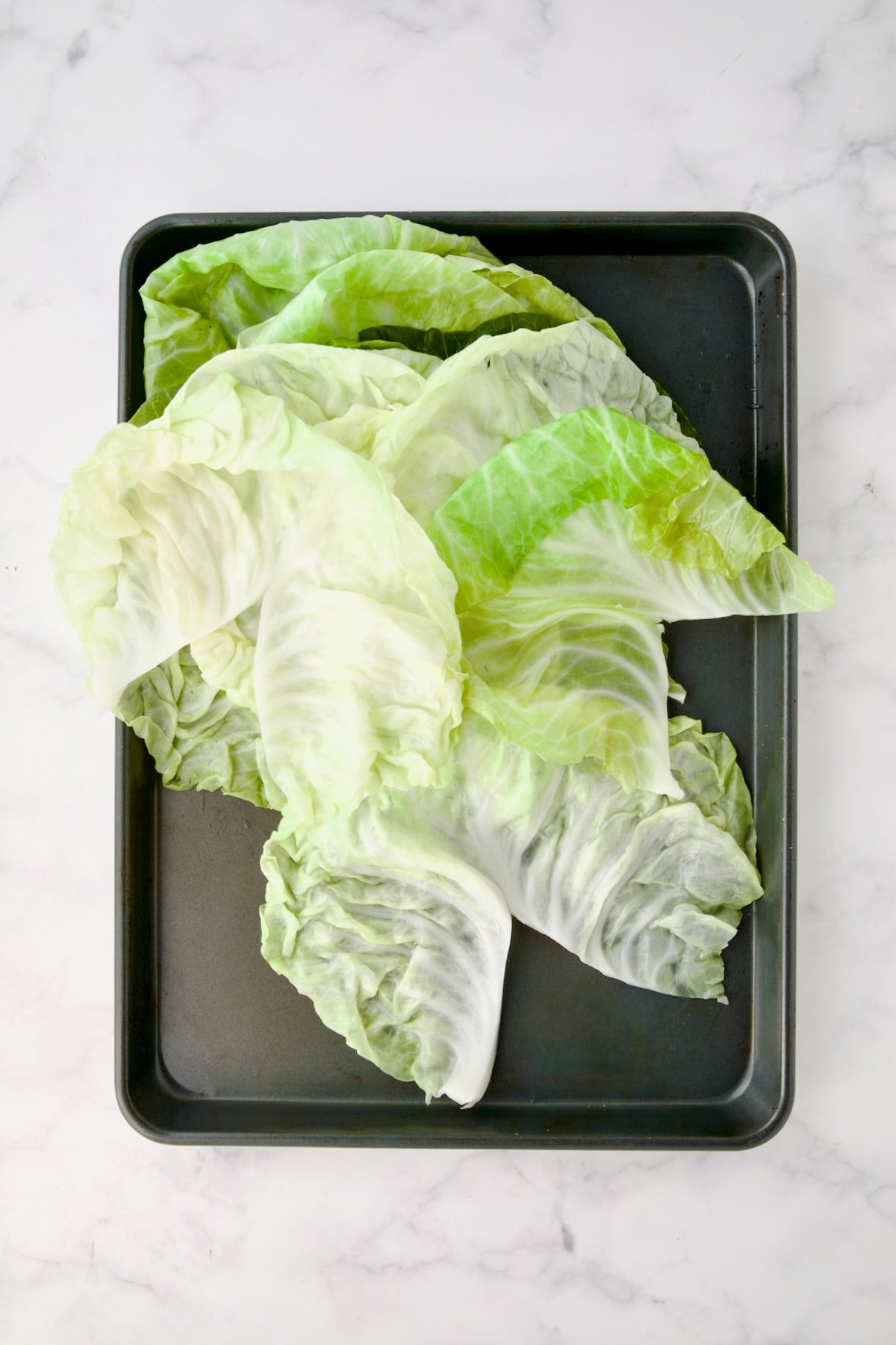 Leaves of cooked cabbage on rimmed baking sheet cut to remove the center ridge to create a V-shape.