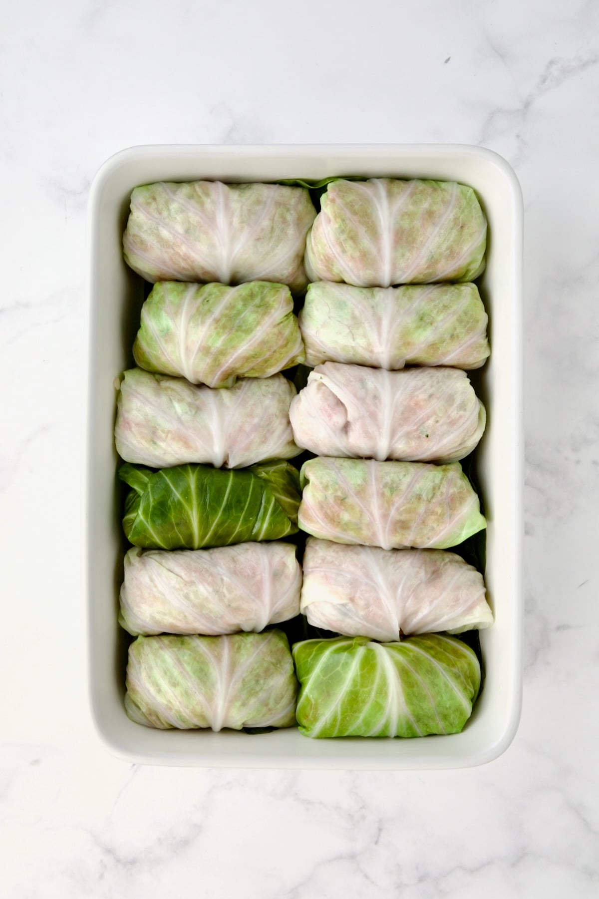 12 filled cabbage rolls in white rectangular baking dish.