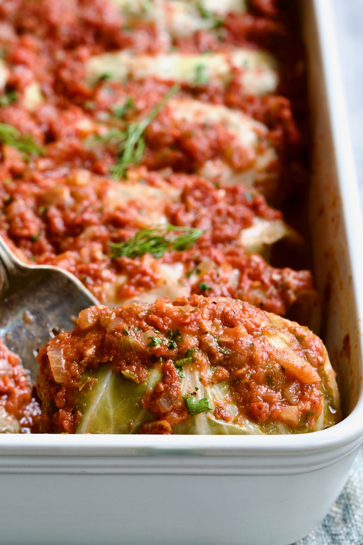 Serving fork picking up a Polish Stuffed Cabbage roll from white baking dish.