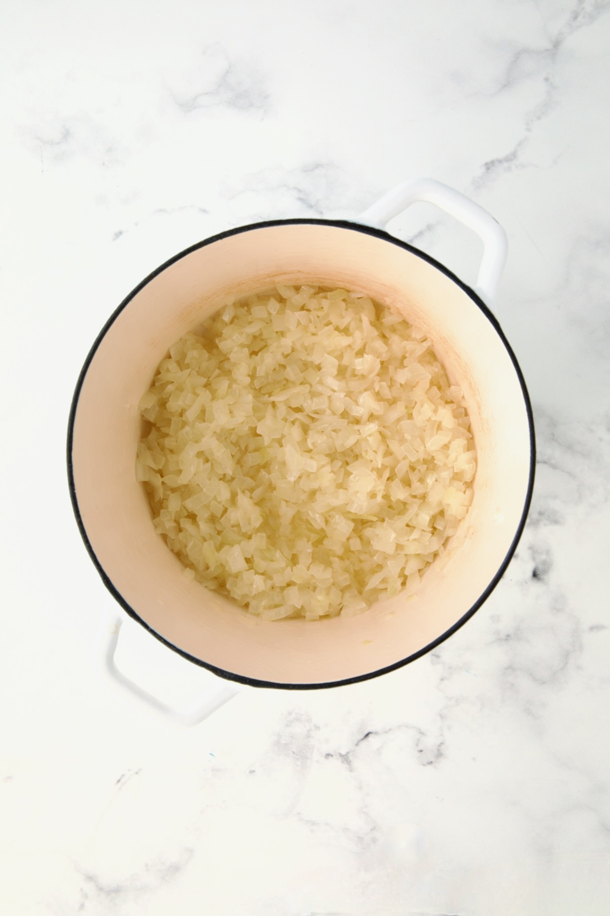 Partially cooked onions in white Dutch oven.