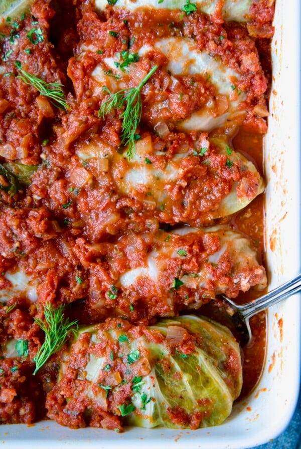Row of four Polish Stuffed Cabbage in white baking dish with serving fork garnished with fresh dill.
