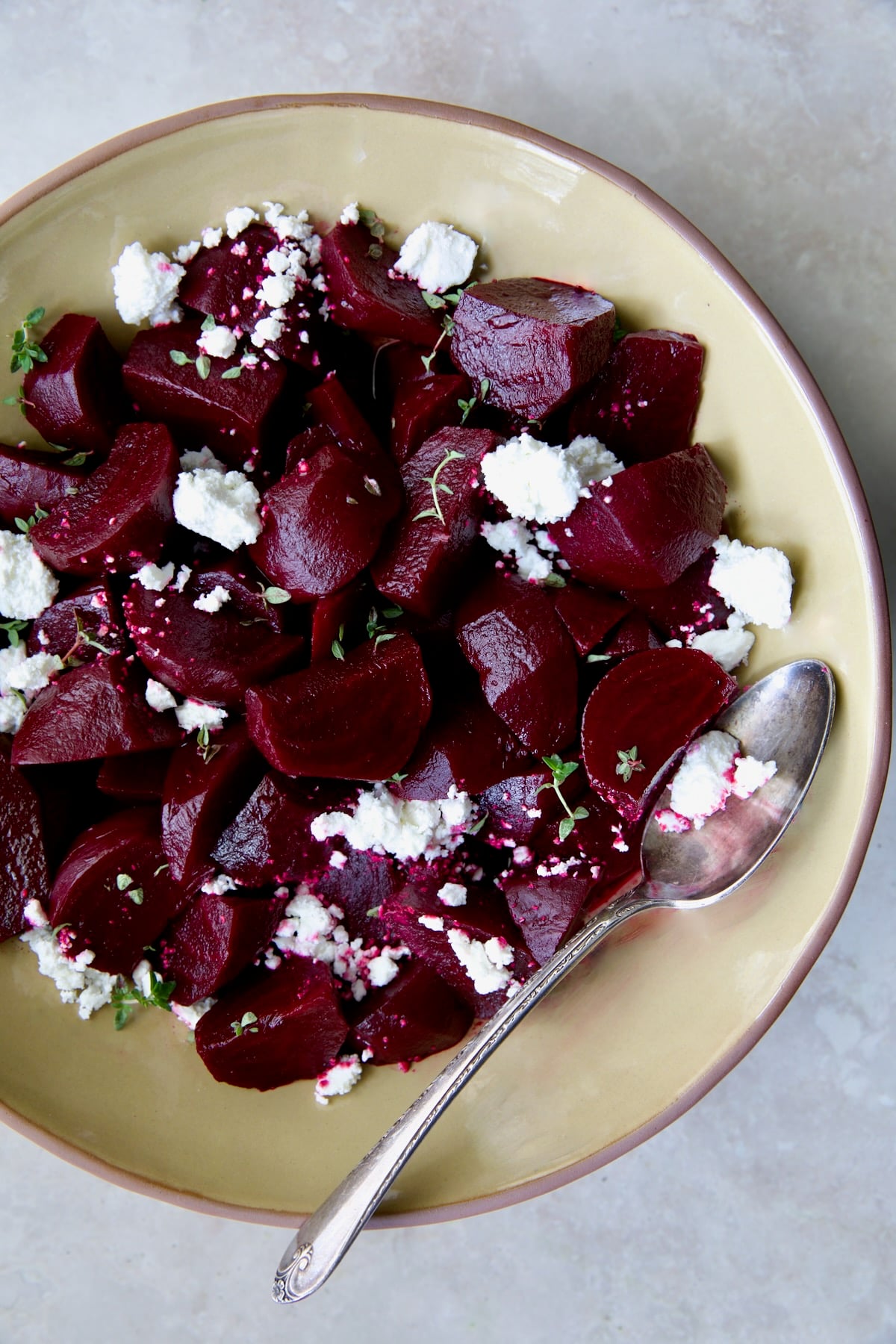 serving bowl with serving spoon sprinkled with goat cheese.