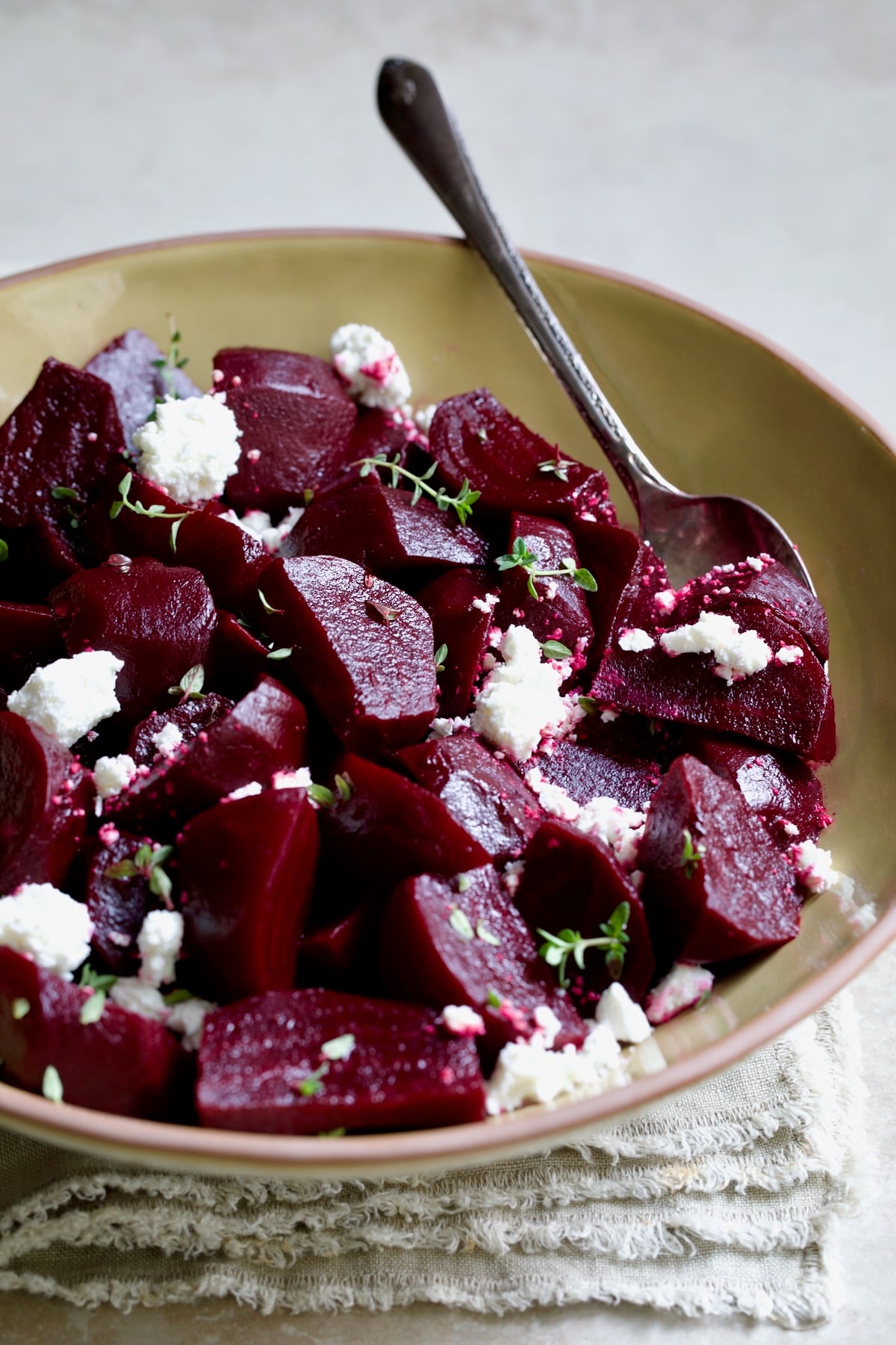 serving bowl with serving spoon sprinkled with goat cheese.
