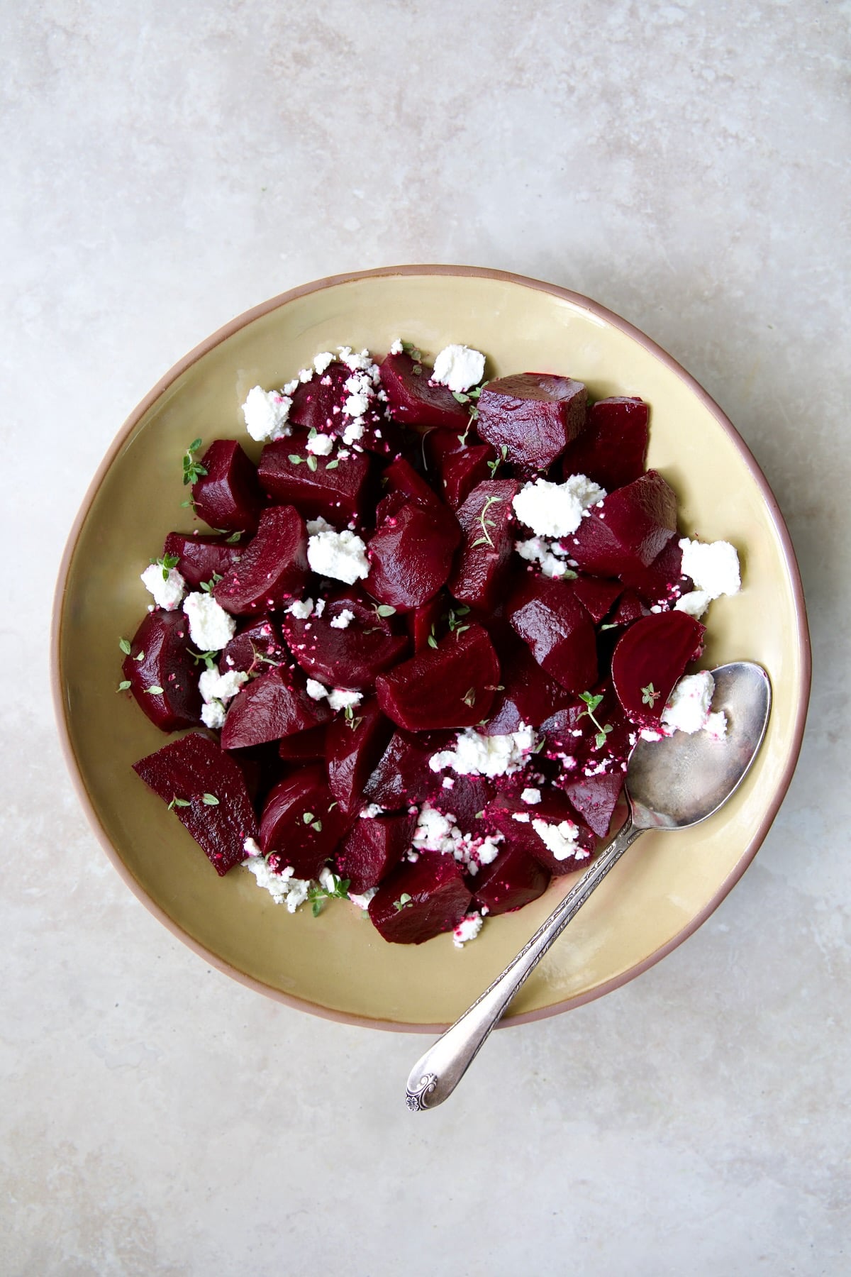 serving bowl with serving spoon sprinkled with goat cheese.