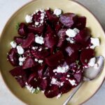 Roasted Beets with Red Wine Glaze in earthenware serving bowl with serving spoon sprinkled with goat cheese.