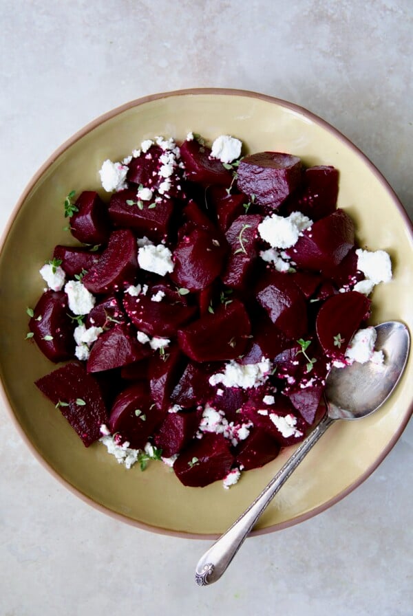 Roasted Beets with Red Wine Glaze in earthenware serving bowl with serving spoon sprinkled with goat cheese.