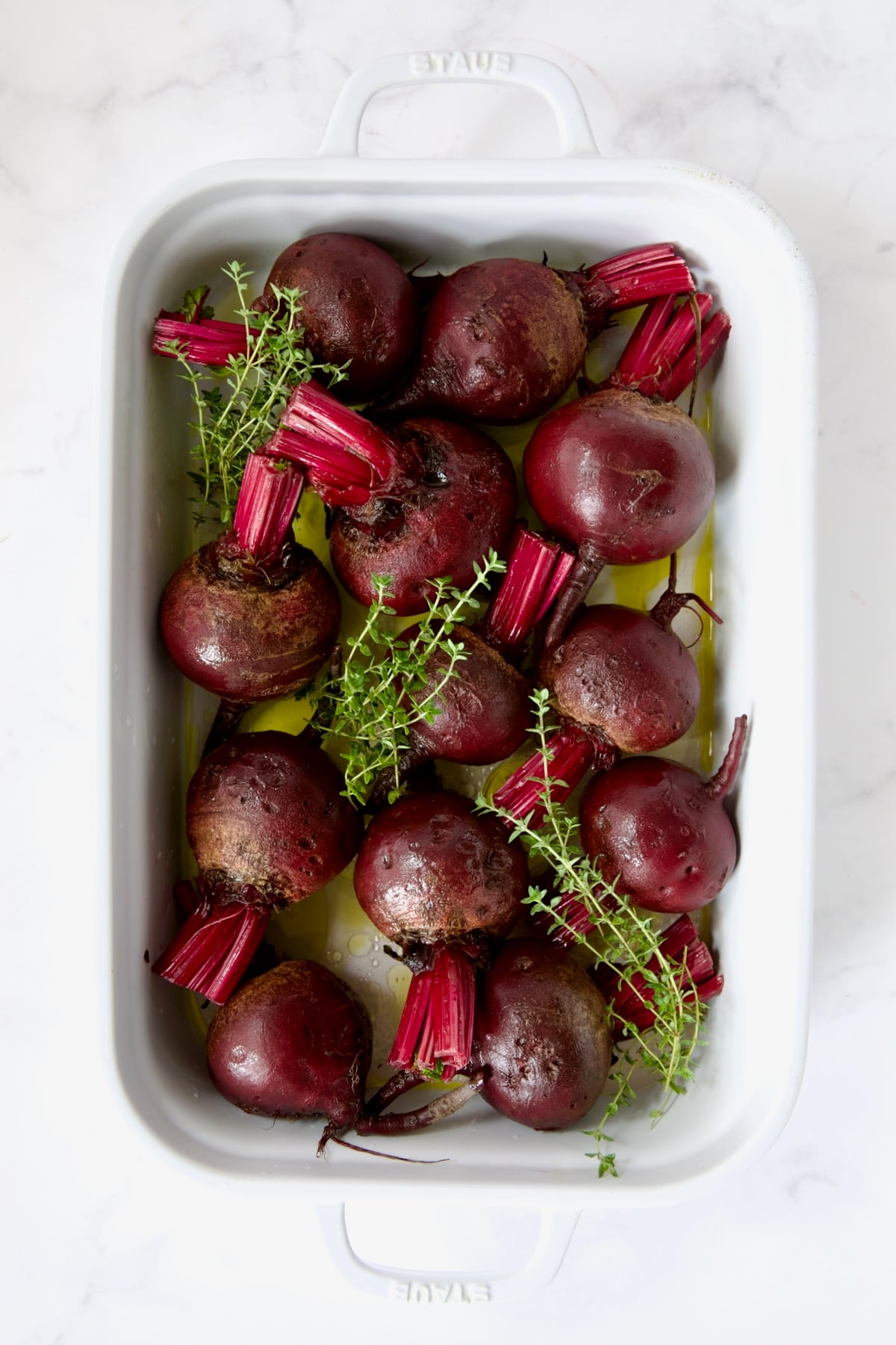 Raw beets and thyme sprigs in white rectangular roasting dish.