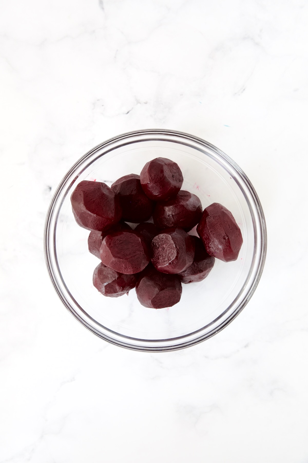 Whole peeled roasted beets in glass bowl.