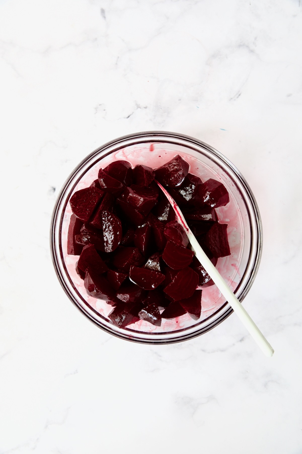 Beets being stirred with red wine glaze in glass bowl.