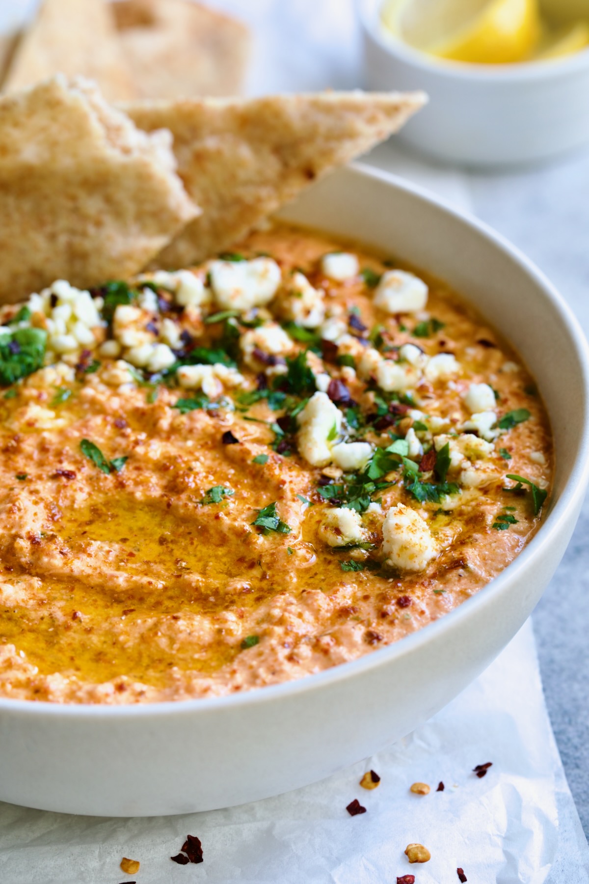 Spicy Feta Dip (Tirokafteri) in white bowl garnished with crumbled feta cheese and parsley surrounded by pita wedges.