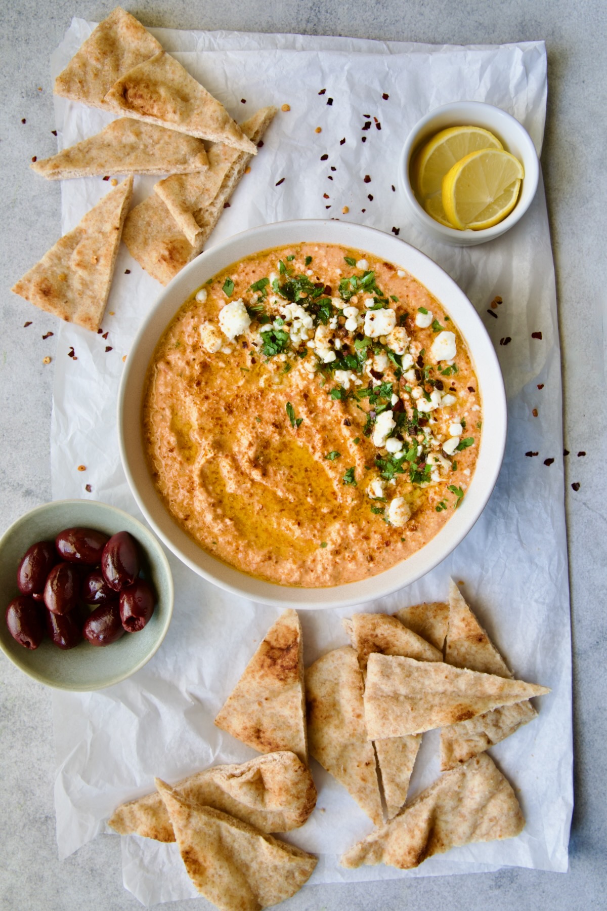 Spicy Feta Dip (Tirokafteri) in white bowl on parchment paper garnished with crumbled feta cheese and parsley surrounded by pita wedges.