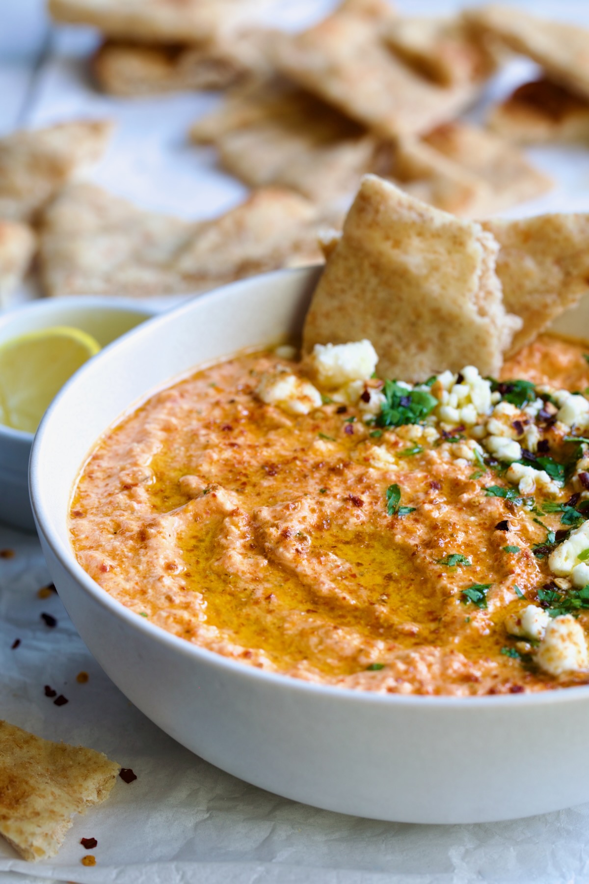 Spicy Feta Dip (Tirokafteri) in white bowl garnished with crumbled feta cheese and parsley surrounded by pita wedges.