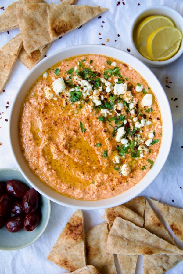 Spicy Feta Dip (Tirokafteri) in white bowl garnished with crumbled feta cheese and parsley surrounded by pita wedges.